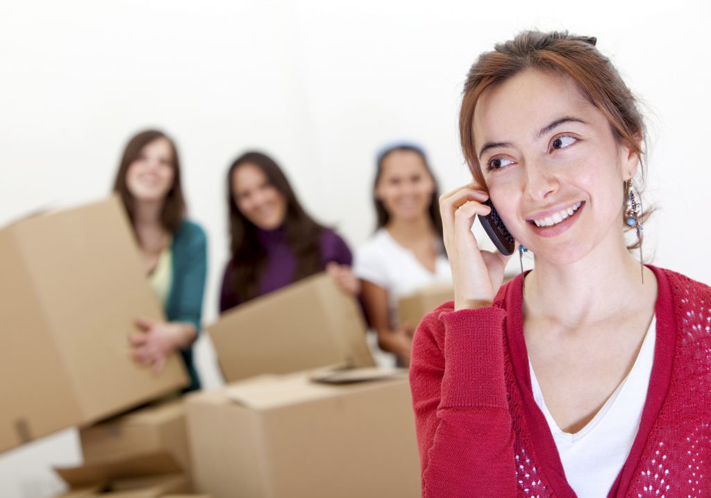 Group of girls calling the moving van while packing in boxes