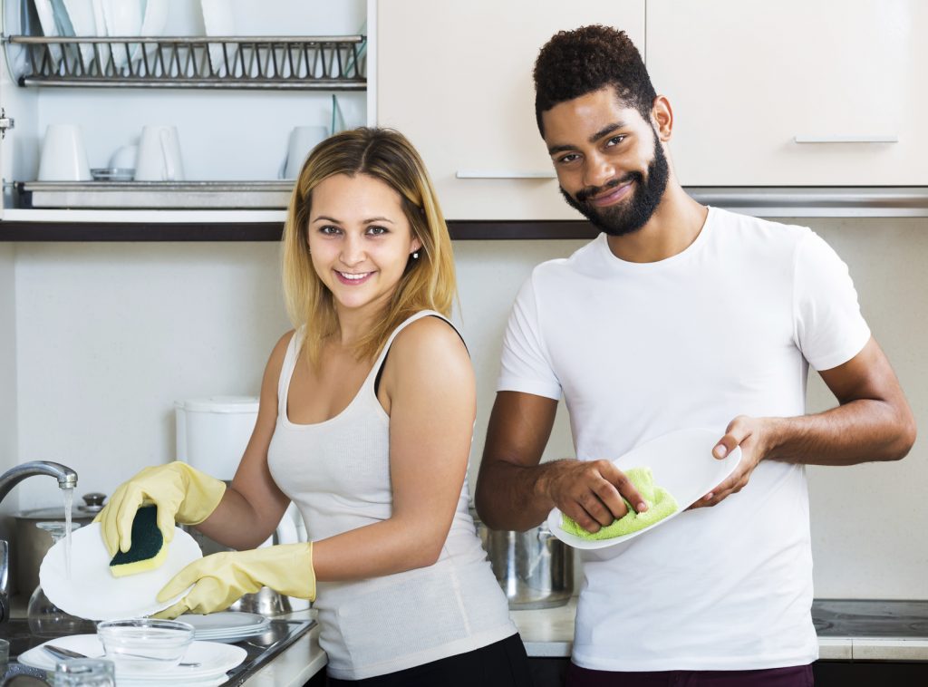 Positive interracial couple cleaning in the kitchen together and smiling