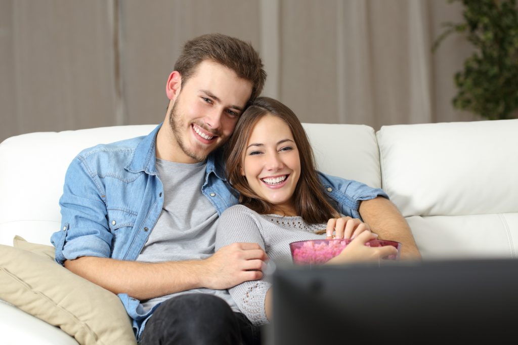 Happy couple watching a movie on tv sitting on a couch at home