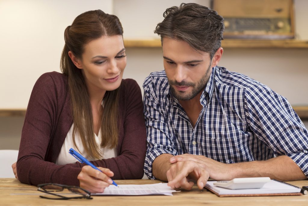 Happy young couple reading and analyzing bills sitting at table. Young couple in casual discussing home economics. Young couple calculating their expenses and incomes.